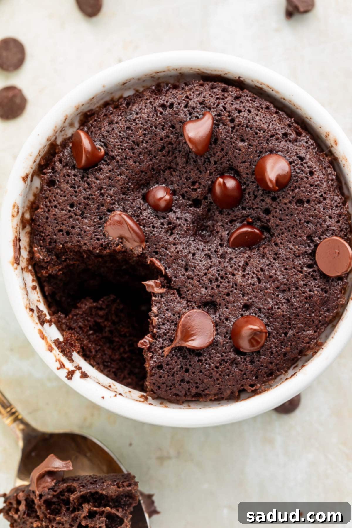 A keto mug brownie topped with keto chocolate chips in a white coffee mug. A spoonful of brownie is missing from the mug.