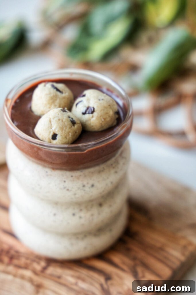 A beautiful close-up of creamy Cookie Dough Blended Oats in a clear glass jar, layered with a rich, dark chocolate ganache and sprinkled with chocolate chips, ready to be enjoyed as a decadent breakfast.