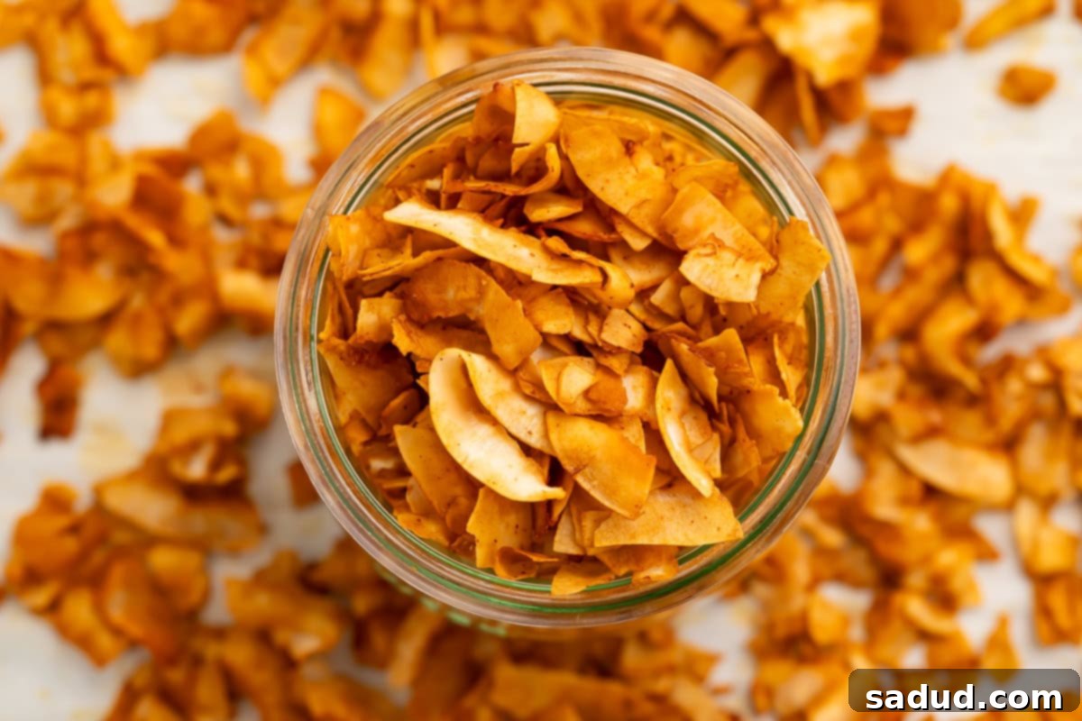 A glass jar of crispy coconut bacon chips on a table surrounded by coconut bacon.