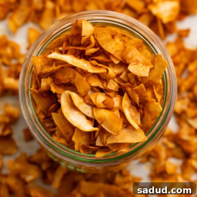 A glass jar of crispy coconut bacon chips on a table surrounded by coconut bacon.