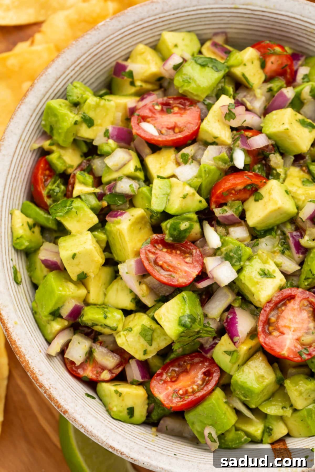 Close-up view of chunky guacamole salad with avocado and cherry tomatoes in a large white bowl.