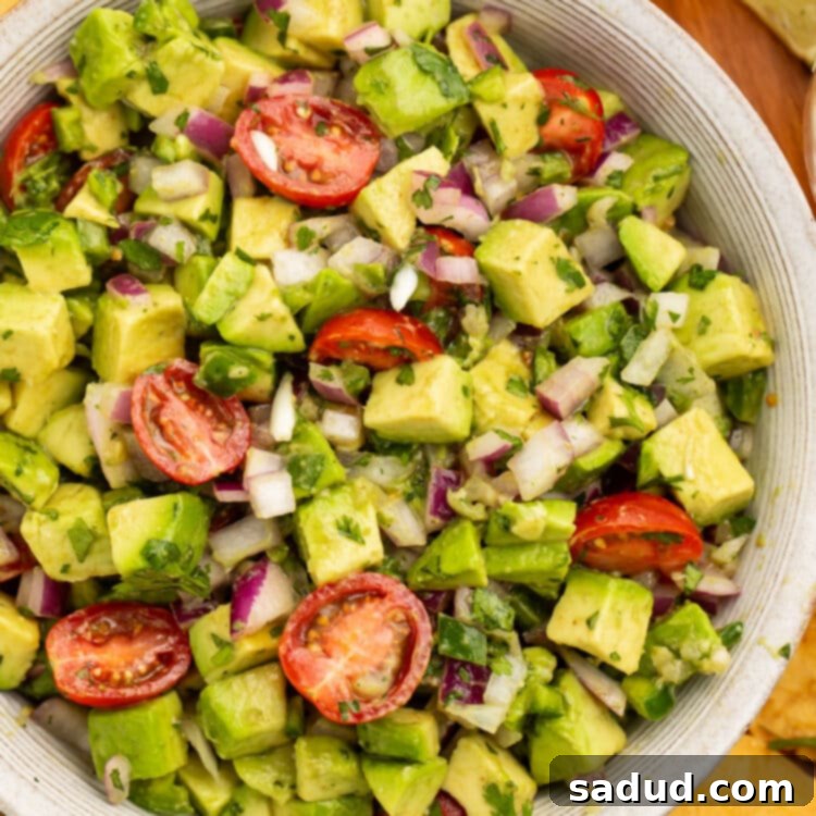 Close-up view of chunky guacamole salad with avocado and cherry tomatoes in a large white bowl.