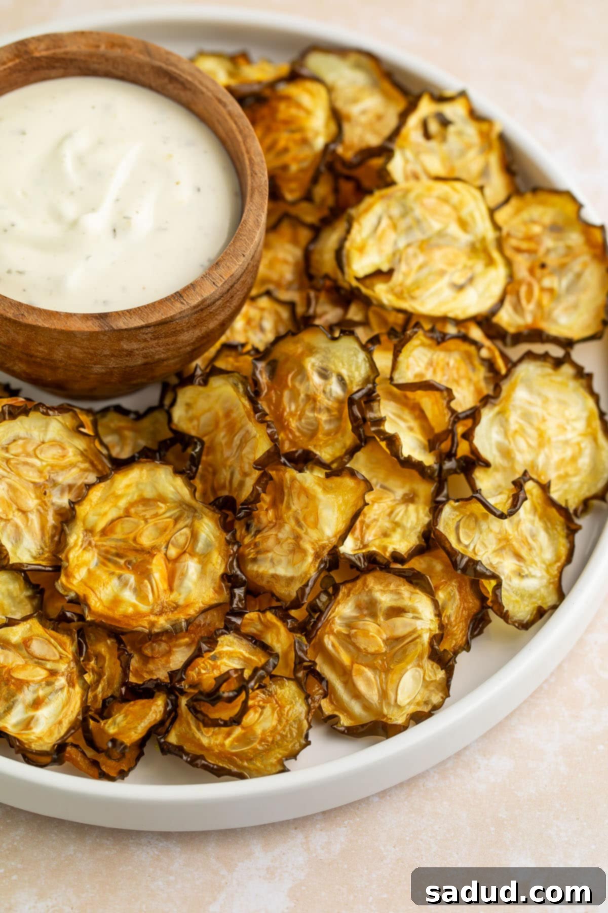 Crispy cucumber chips arranged around a bowl of ranch dressing on a large rimmed plate.