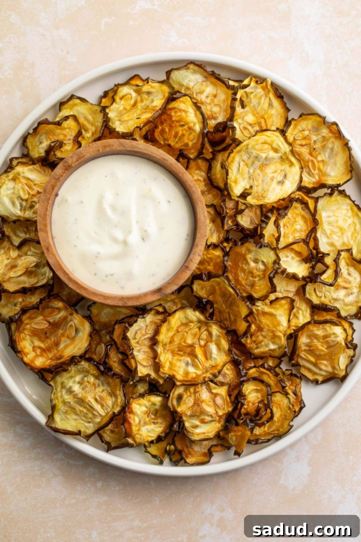 Crispy cucumber chips arranged around a bowl of ranch dressing on a large rimmed plate.