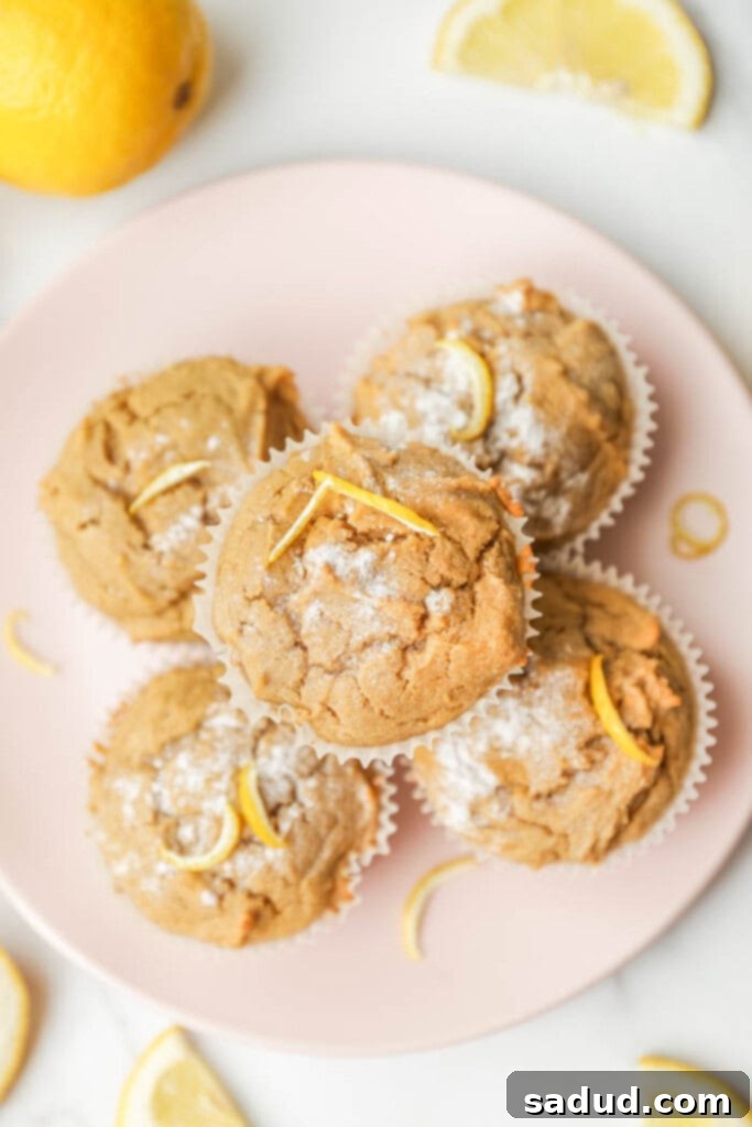 Freshly baked gluten-free lemon muffins on a white plate, garnished with lemon zest and a dusting of powdered sugar