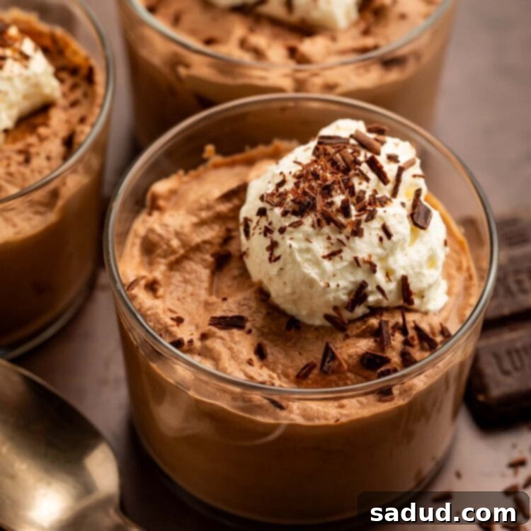 Three glass cups of keto chocolate mousse topped with keto whipped cream and chocolate shavings.