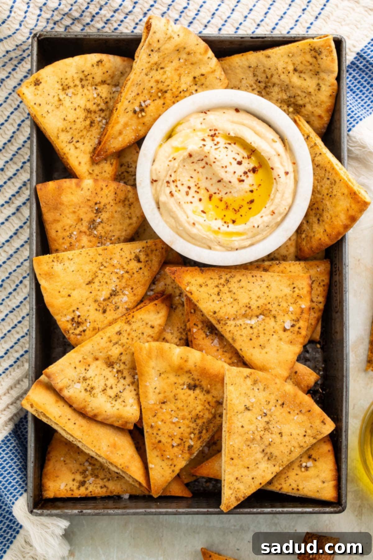 Homemade pita chips in a pan with a small dipping bowl of hummus.
