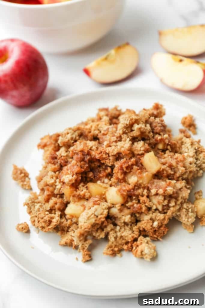 A single serving of freshly baked vegan apple crisp on a small plate, showcasing the golden-brown, crumbly topping and the warm apple filling beneath.
