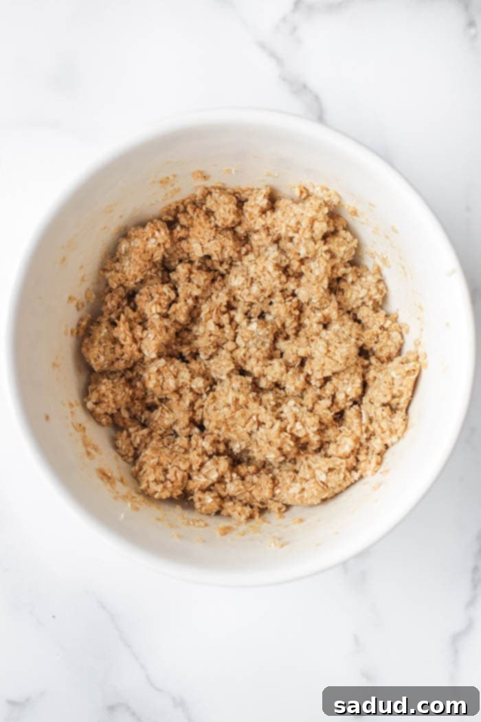 Topping ingredients, including rolled oats and cashew butter, being mixed in a bowl to create a crumbly texture.
