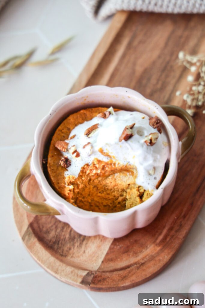 A close-up shot of a single serve pumpkin pie with a spoon scooping out a bite, topped with whipped cream and nuts.