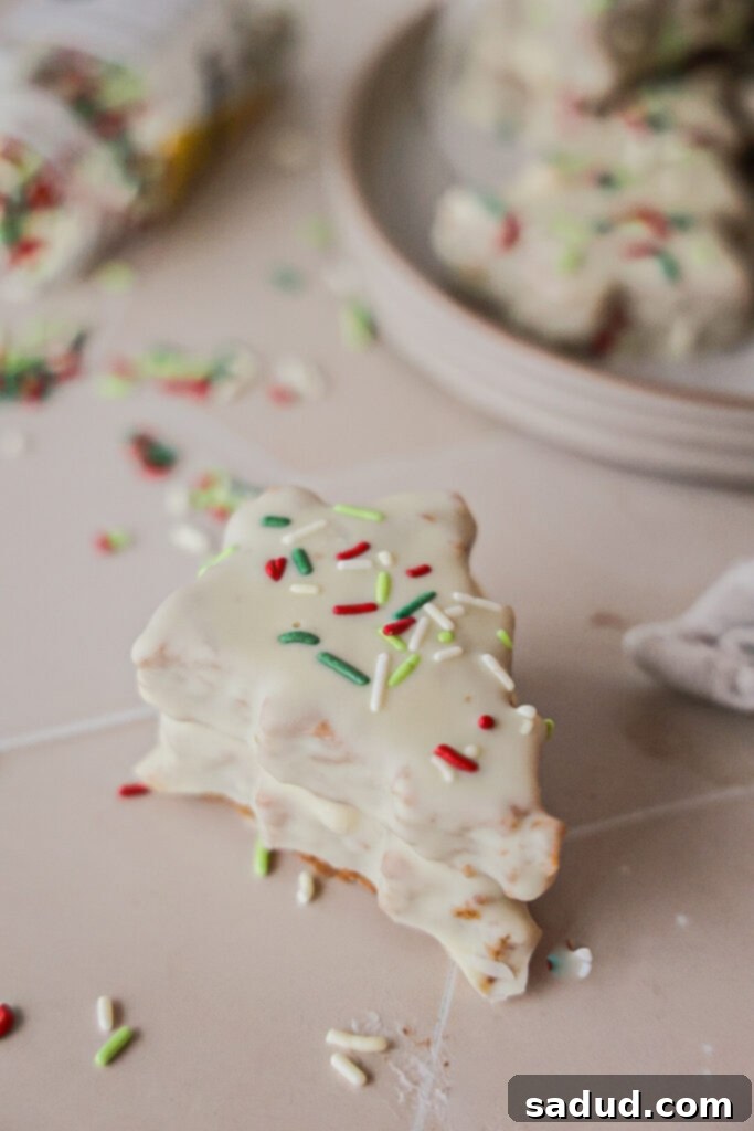 Two festive, healthier Little Debbie's style Christmas tree cakes, decorated with green frosting and colorful sprinkles, on a rustic wooden surface with holiday lights in the background.