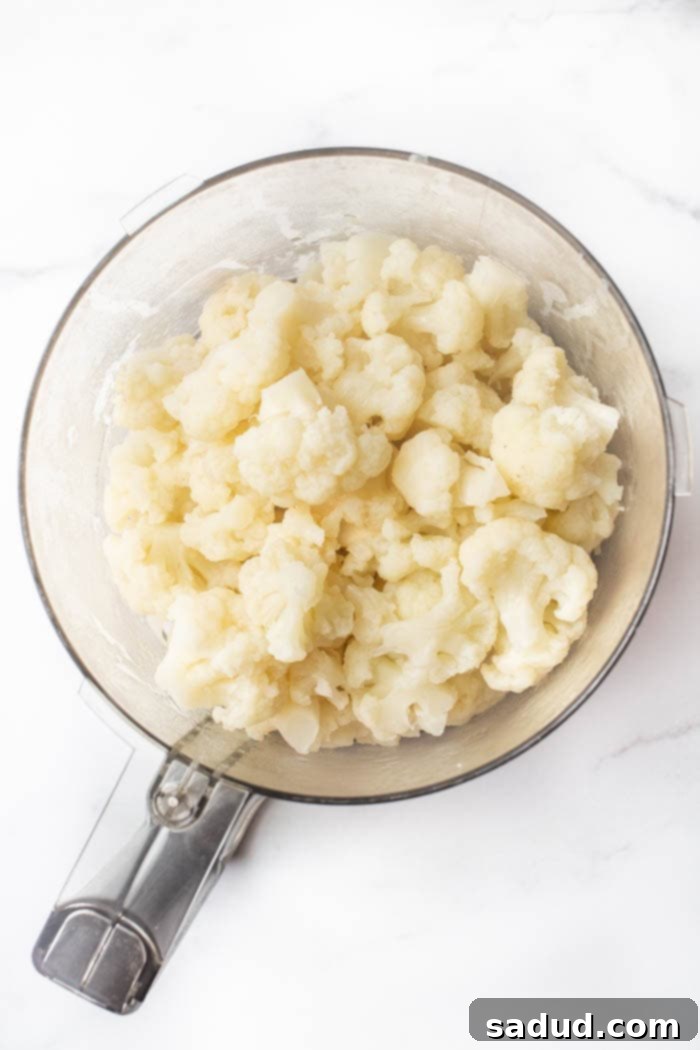 Steamed cauliflower being pulsed in a food processor to achieve a crumb-like texture, then squeezed in a cheesecloth to remove moisture.