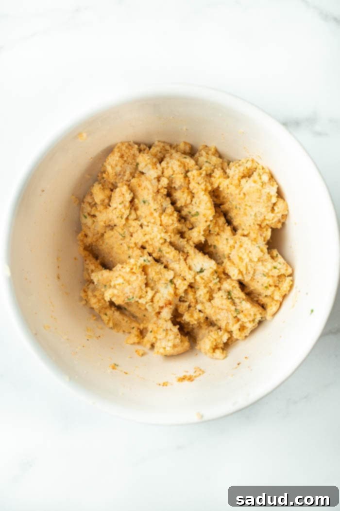 Mixing cauliflower crumbs with Parmesan cheese and spices in a large bowl to form a dough-like mixture for the chips.
