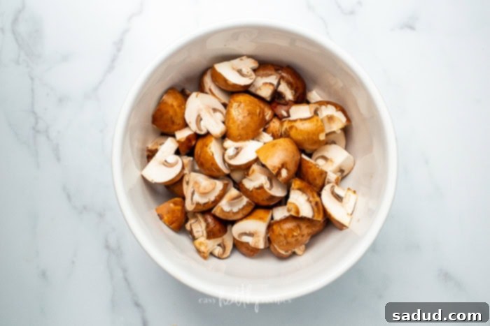 A white bowl full of uncooked and unseasoned mushrooms on a white counter