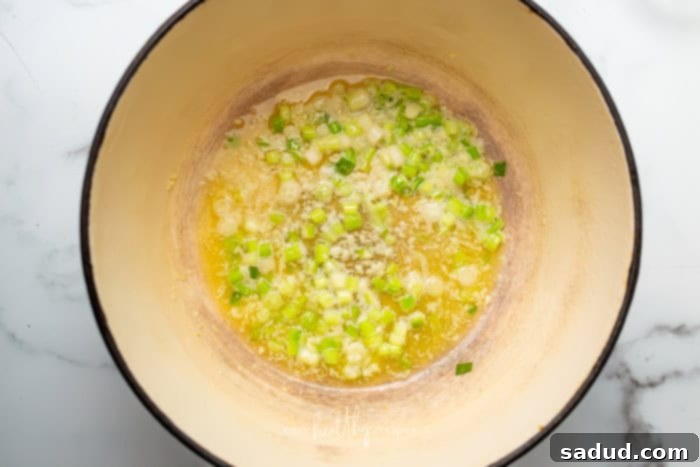Minced garlic and chopped white parts of green onions sautéing in melted butter in a stockpot, releasing their aromatic flavors.