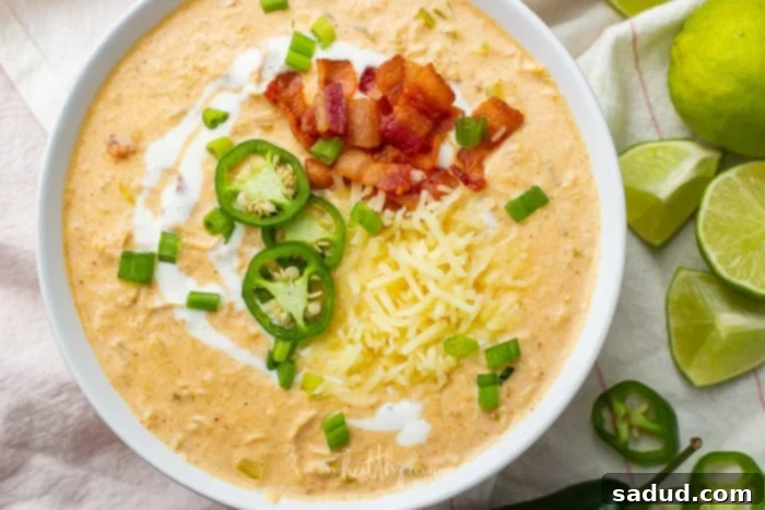 A full bowl of keto white chicken chili, garnished with crispy bacon and fresh jalapeno slices, accompanied by lime wedges for serving, highlighting the final presentation.