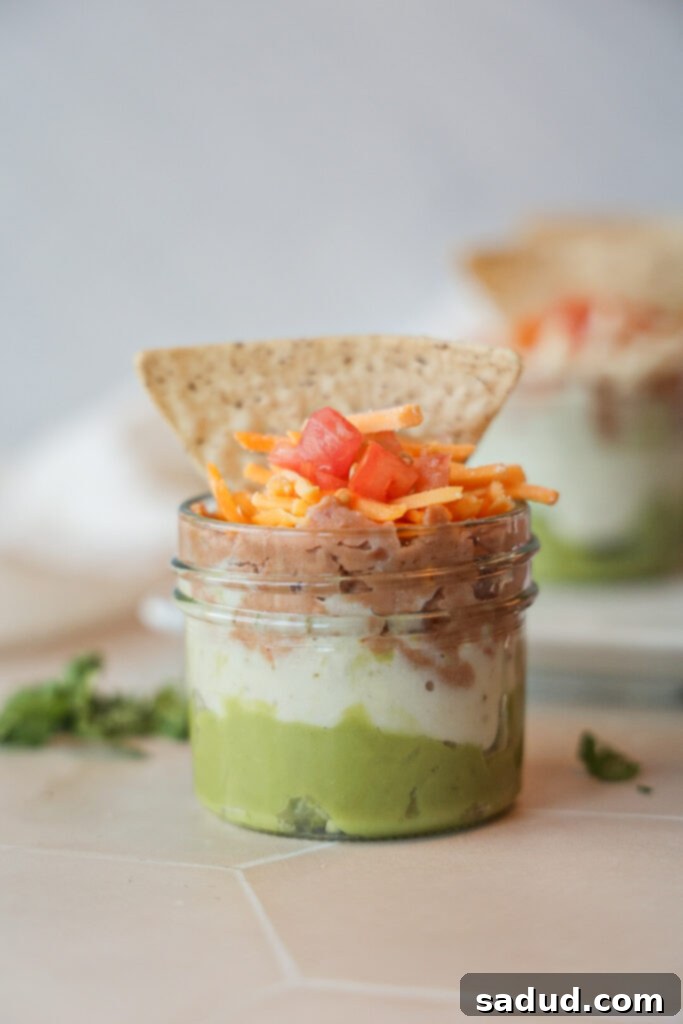 A vegan 7 layer dip cup with a tortilla chip in it.
