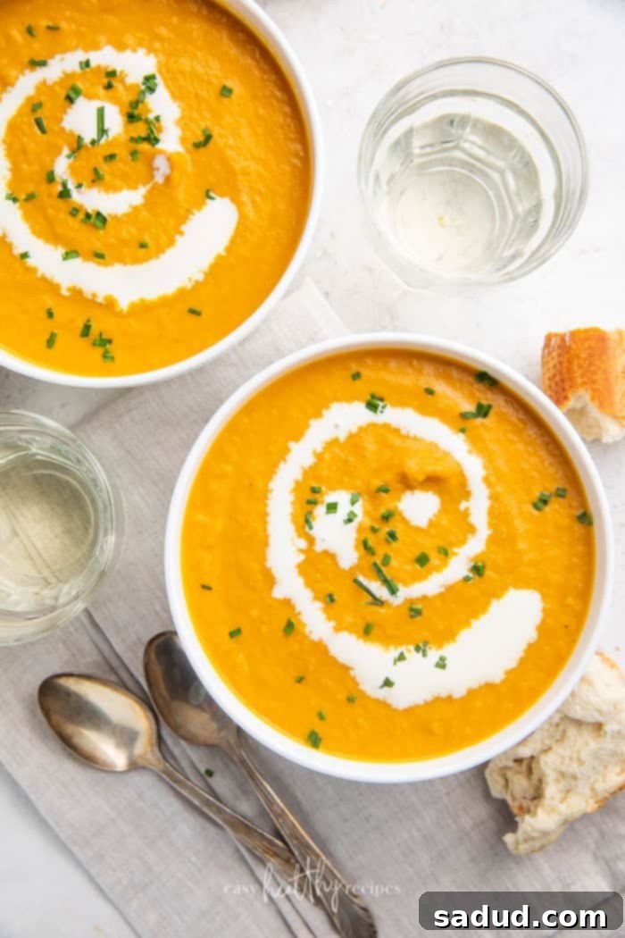 Two cozy bowls of pumpkin bisque on a rustic wooden table, surrounded by spoons, glasses, and freshly baked bread.