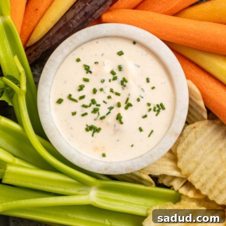 A bowl of buffalo ranch dressing surrounded by carrot sticks, celery sticks, and potato chips on a pan.