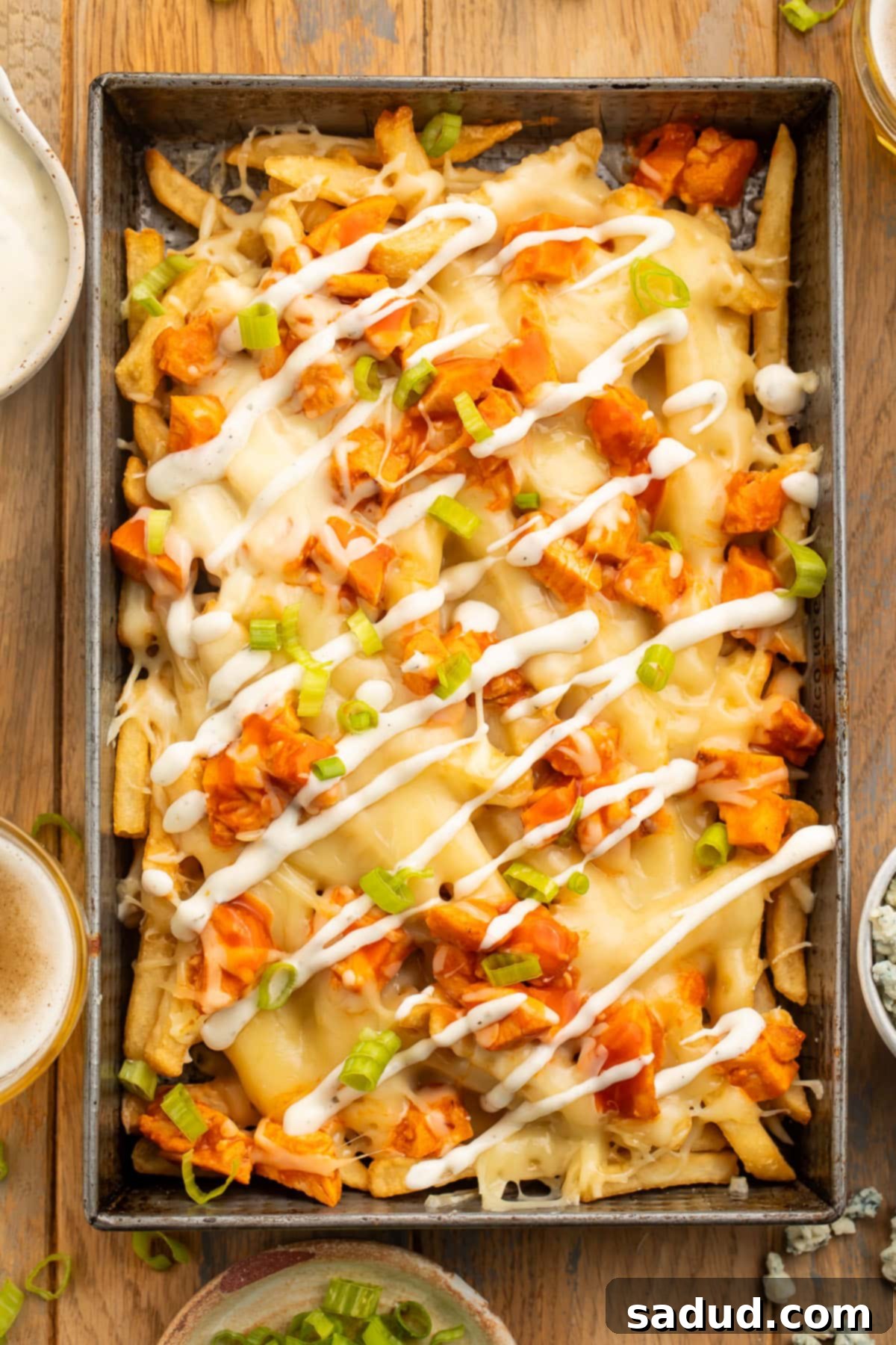 Overhead view of a rectangular baking pan holding french fries topped with buffalo chicken, green onions, and a ranch dressing drizzle.