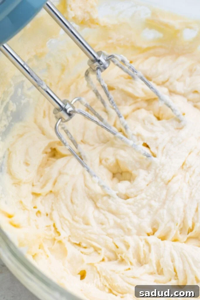 Keto cream cheese frosting being mixed in a large bowl with an electric mixer, showing its creamy texture.