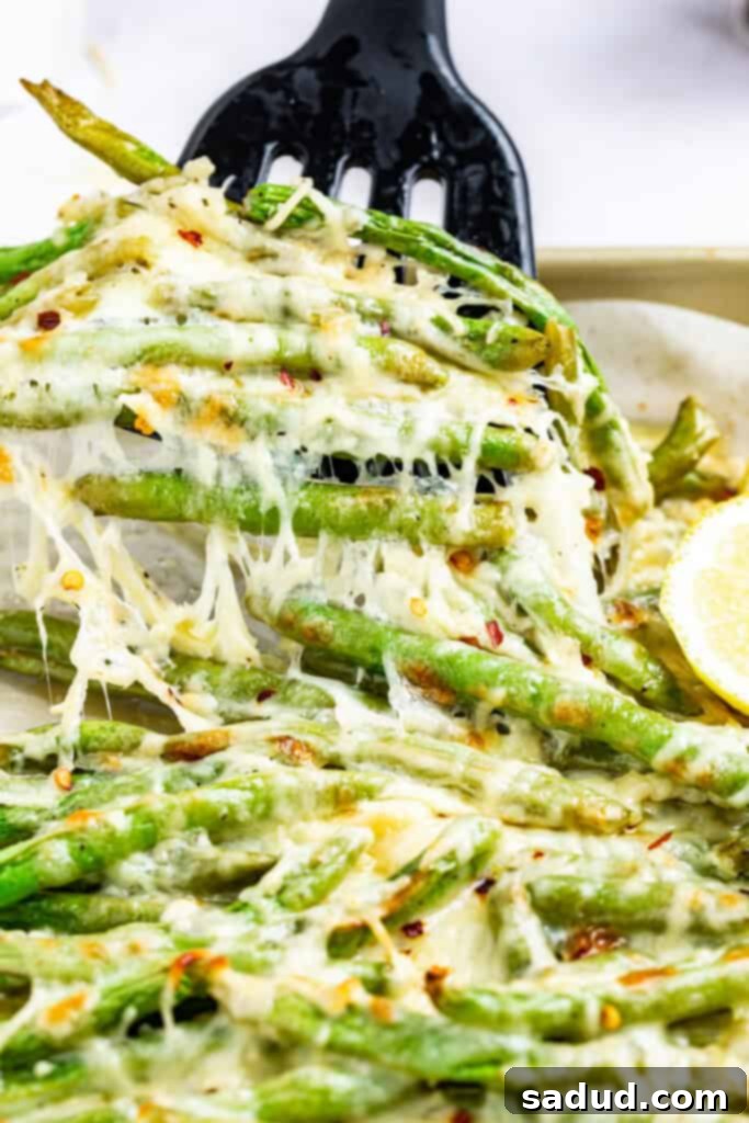 Baked Keto Cheesy Green Beans 3 keto green beans being lifted off a baking sheet with a spatula