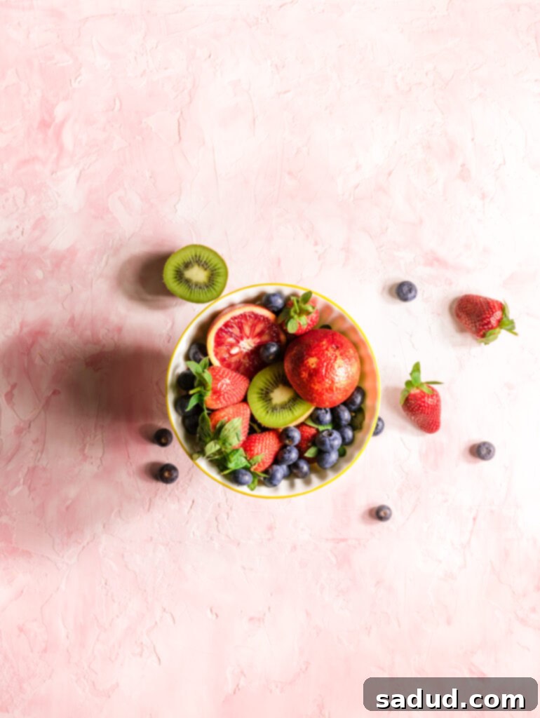 A vibrant fruit bowl on a pink background, representing healthy vegan high-protein snacks.