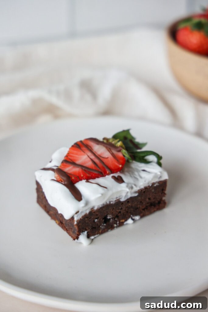Gluten-free paleo brownies topped with fresh strawberries and a dollop of creamy coconut whipped cream, ready to be served.