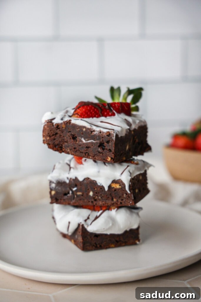 A stack of fudgy paleo brownies with coconut whipped cream and sliced fresh strawberries, garnished with sea salt.
