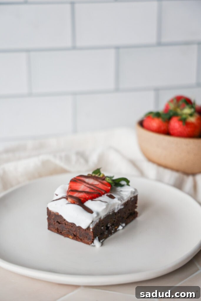 Close-up of fudgy paleo brownies with whipped cream and fresh strawberries, showing the rich texture and delicious toppings.