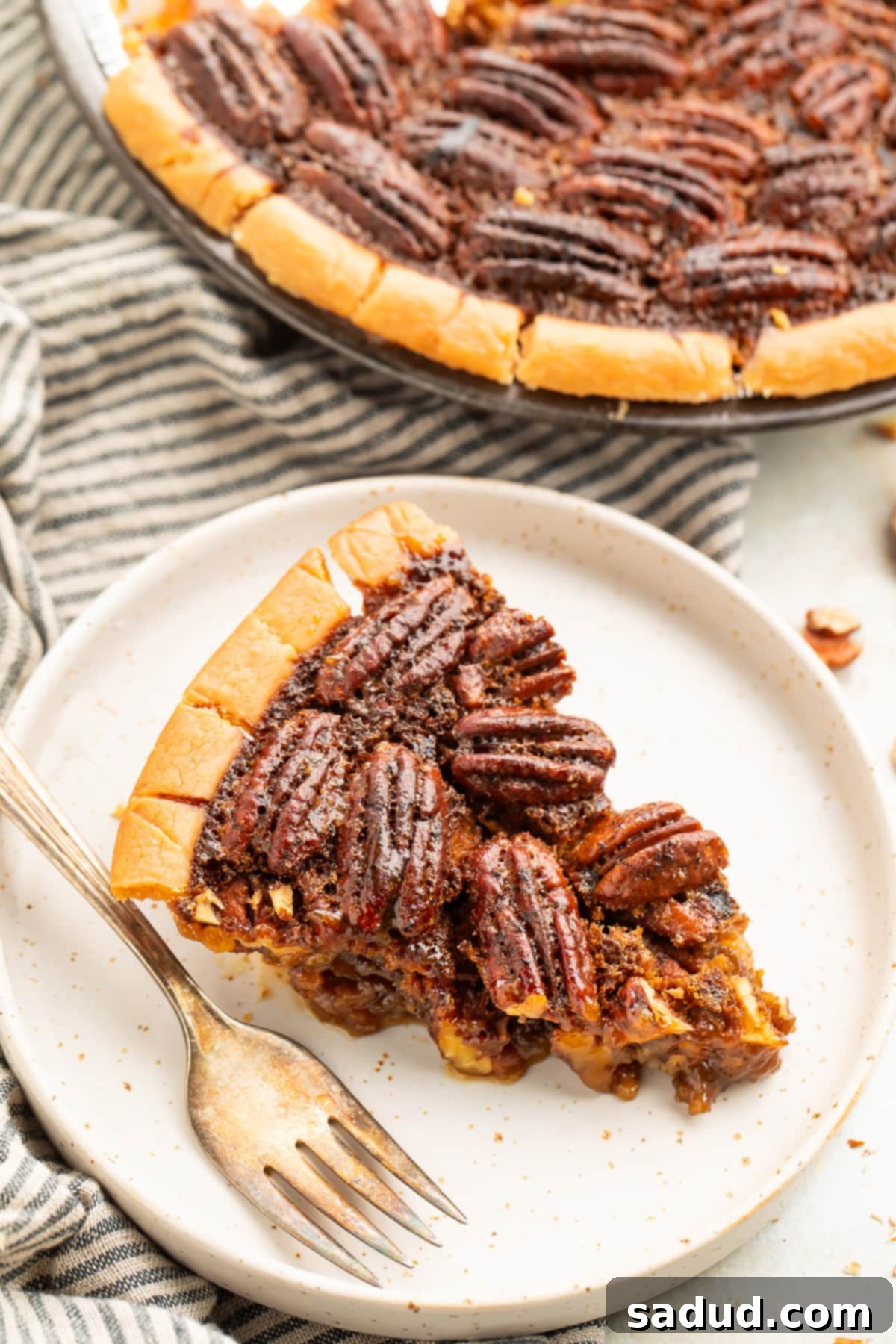 A wedge slice of gluten free pecan pie on a plate next to the remaining pie in a pie plate, ready to be served.