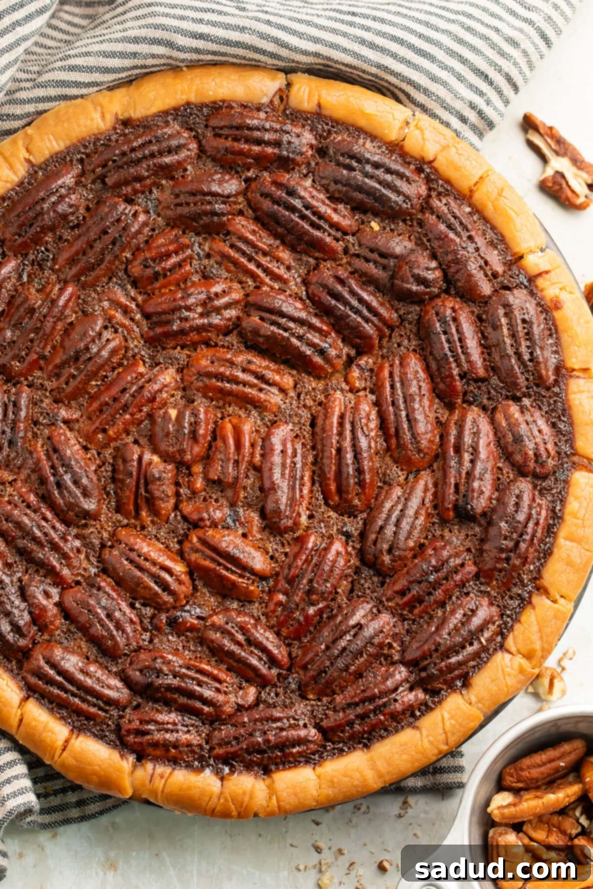 Top down view of a whole gluten free pecan pie in a pie plate on a neutral table, showcasing its golden crust and nutty topping.
