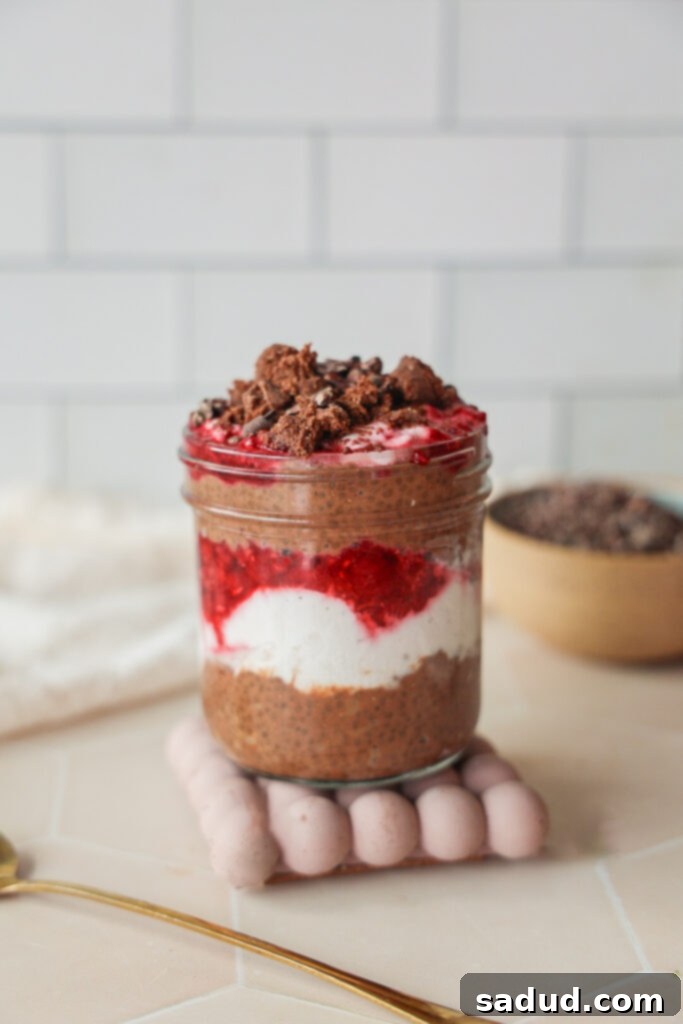A jar of chocolate chia seed protein pudding with coconut yogurt and raspberries, garnished with a brownie ball.