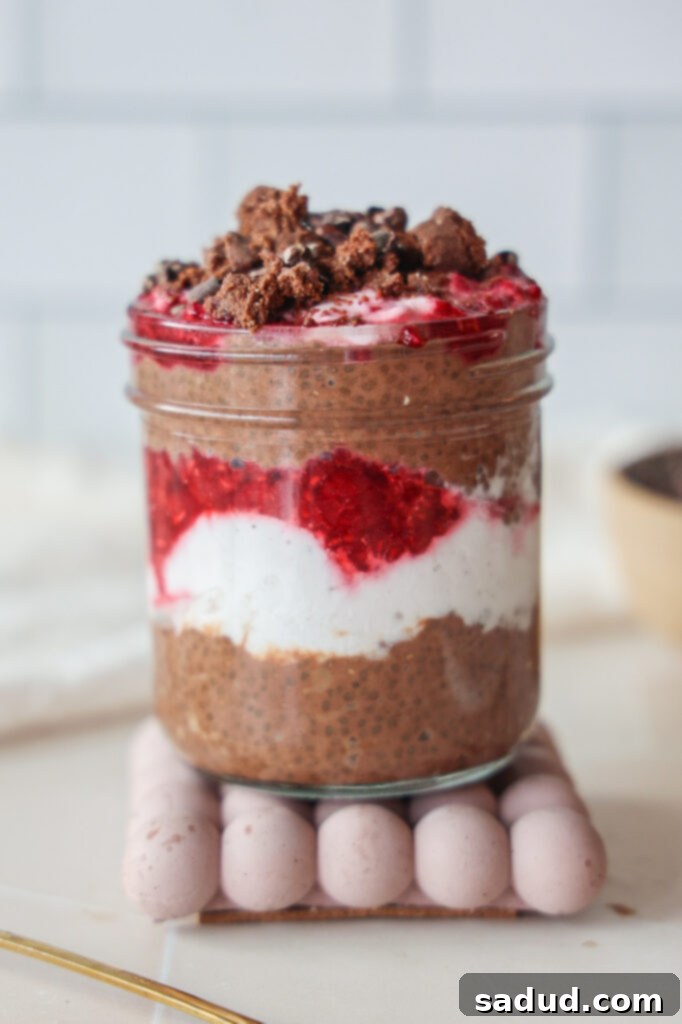 A close-up of a layered jar of chocolate chia seed protein pudding with coconut milk, raspberries, and yogurt.