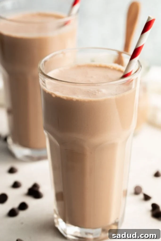 Two glasses of velvety keto chocolate milk surrounded by chocolate chips, looking rich and inviting.