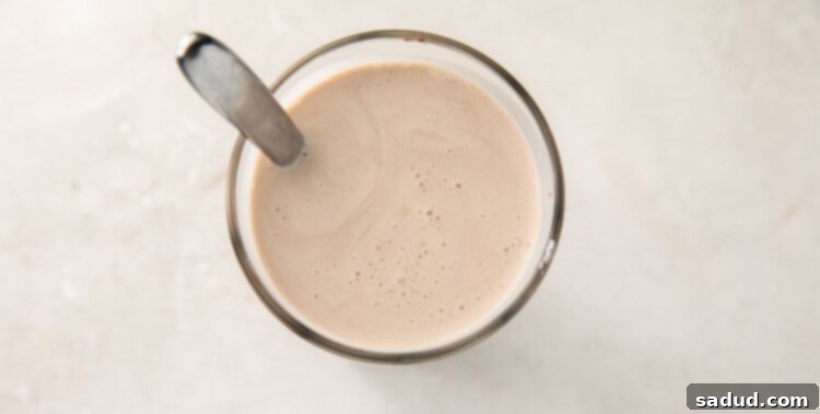 A glass of keto chocolate milk being stirred with a silver spoon, showing the creamy texture.