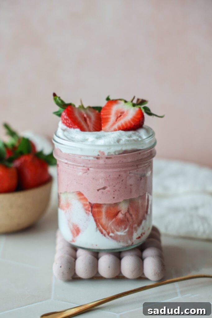 A jar of healthy strawberry yogurt mousse with a dollop of coconut whipped cream on top, garnished with a fresh strawberry.