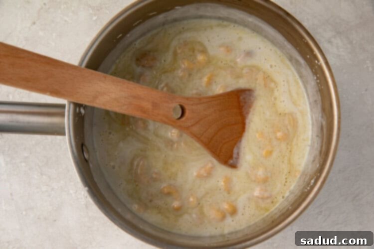 Vegan creme brulee base in a small saucepan with a wooden spoon, after adding sugar and vanilla