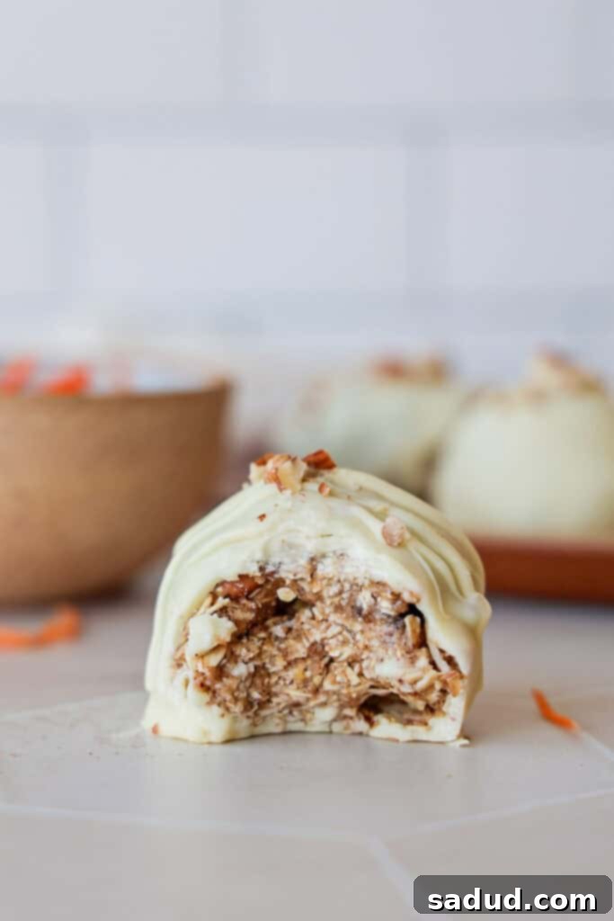 A healthy carrot cake bite covered in white chocolate with a bite taken out, revealing the textured interior of oats, carrots, and nuts.