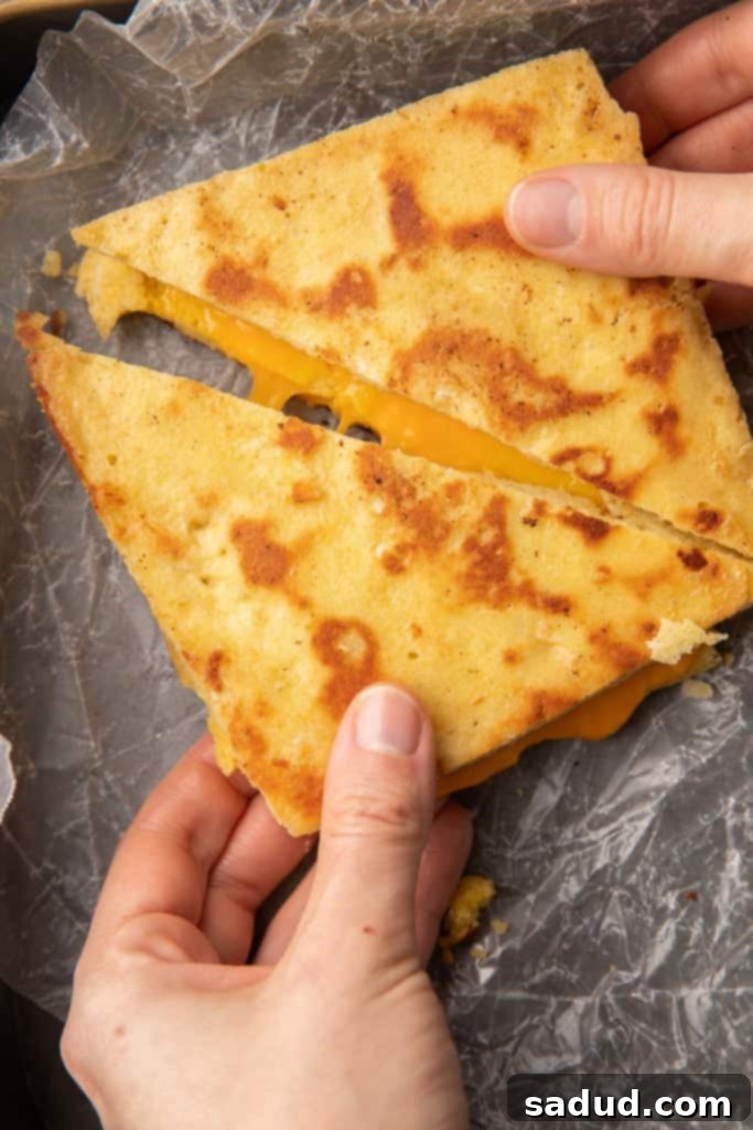 Two hands pulling apart slices of keto grilled cheese made with keto bread, showcasing the melted cheese pull