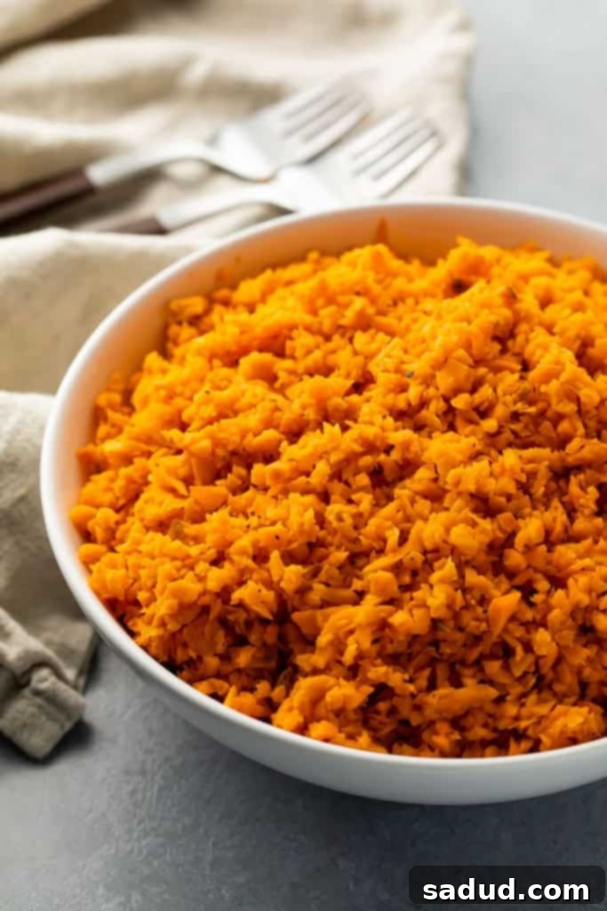 Close-up of bright orange sweet potato rice in a white bowl, garnished with fresh herbs.