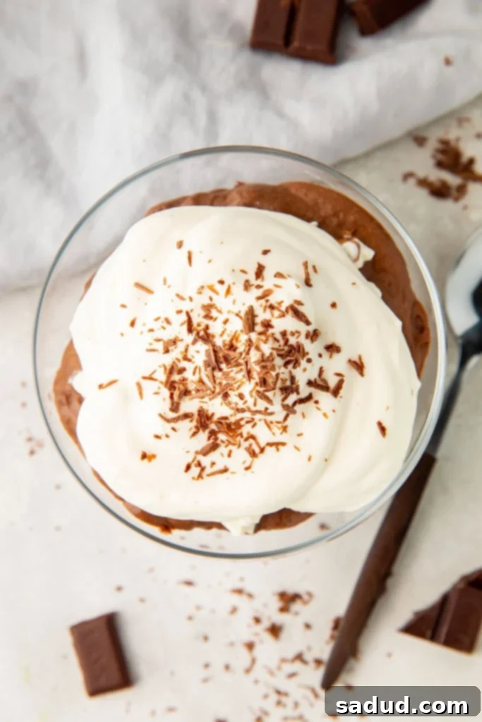 A glass dish filled with thick, rich keto chocolate pudding, generously topped with fluffy keto whipped cream and delicate chocolate shavings, ready to be enjoyed.