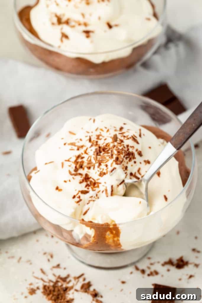 A second close-up view of a glass dish filled with rich keto chocolate pudding, artfully garnished with a swirl of sugar-free whipped cream and delicate chocolate shavings, highlighting its inviting texture.