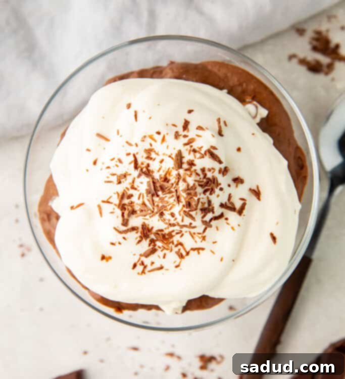 Glass dish of keto chocolate pudding topped with keto whipped cream and chocolate shavings, showcasing its rich, dark color and smooth texture.