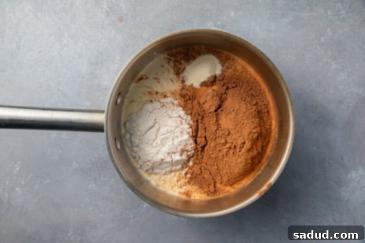 Cocoa powder, heavy cream, swerve, xanthan gum, and salt in saucepan, ready to be whisked for keto chocolate pudding.