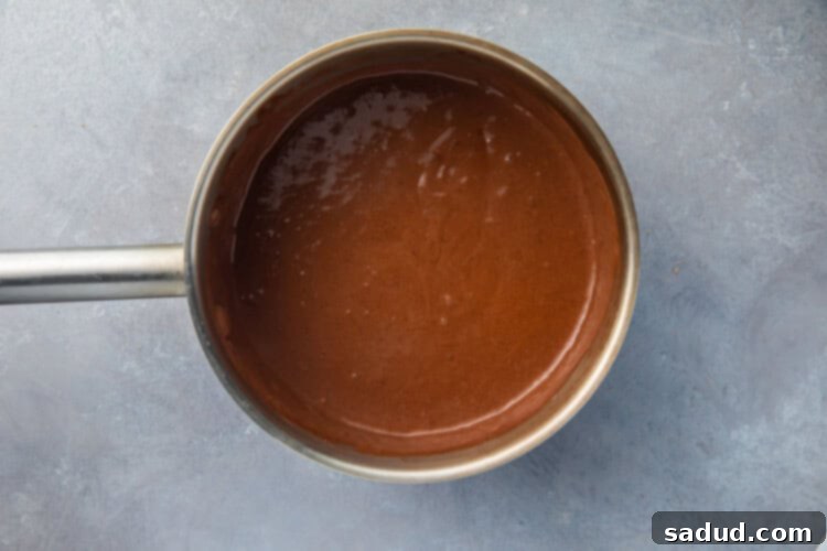 Liquid keto chocolate pudding mixture simmering gently in a saucepan, showing its smooth, thickening consistency.