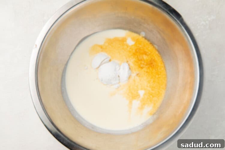 Ingredients for keto whipped cream (heavy cream, vanilla, Swerve) in a metal mixing bowl, ready for whipping.
