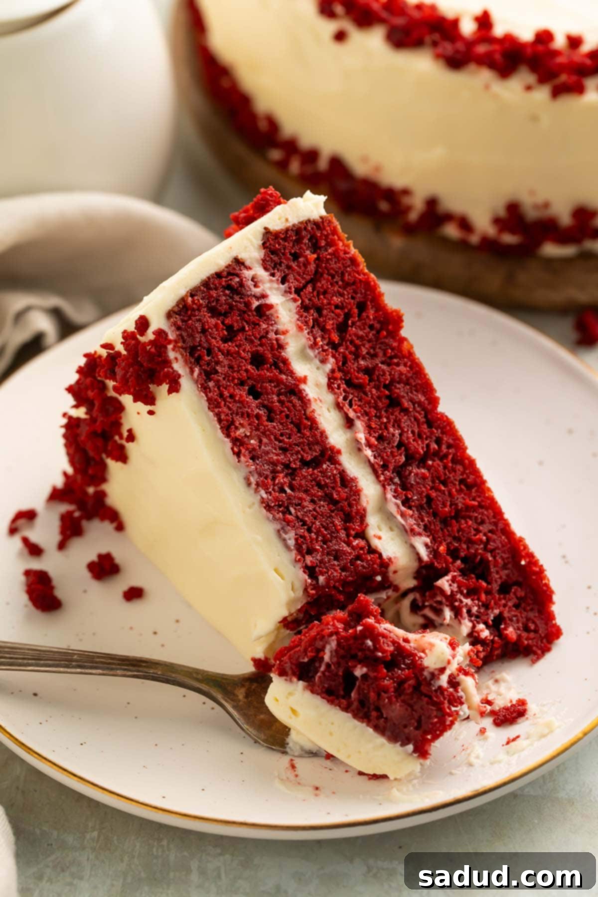 Keto Red Velvet Cake 2 A slice of keto red velvet cake with keto cream cheese frosting on a plate. A bite of red velvet cake rests on a fork sitting on the plate.