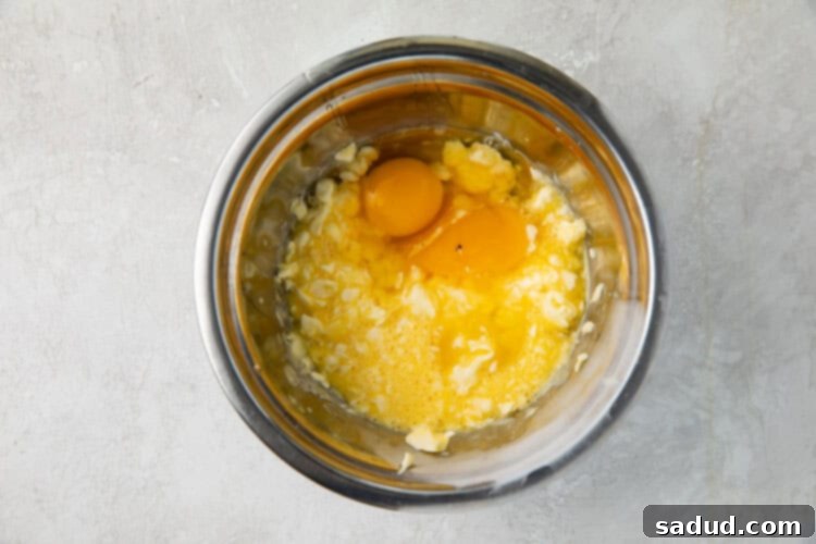 Eggs and butter being beaten in a silver mixing bowl.