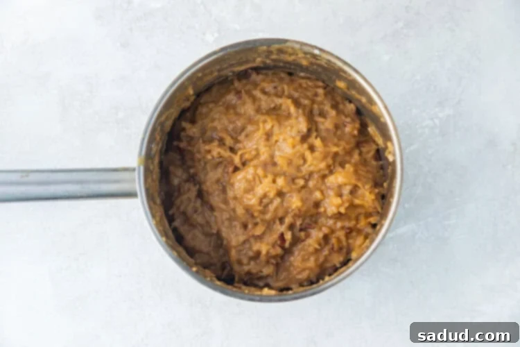 German chocolate cake frosting with coconut and pecans in a silver saucepan, ready to be cooled.